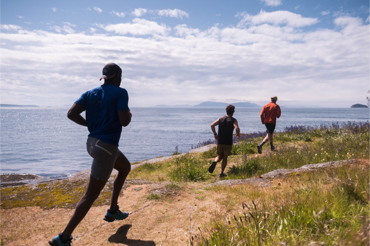 Image shows runners on a coastal trail with water and distant islands in the background.